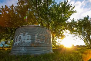 graffiti on a metal cylinder that says, :Love Life" as the sun is setting behind it