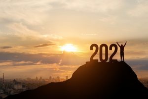 Large 2021 numbers silhouetted on a hilltop with the sun rising behind it and a person standing tall as the number 1