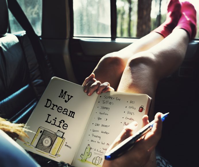 a woman sitting in a car with her feet resting on the opened window as she writes in her journal that has a photo of a camera with the words, My Dream Life