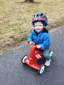 a little boy with Rothmund-Thomson Syndrome, wearing a helmet and riding on a red scooter bike