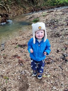a toddler with a blue coat and white hat near a river