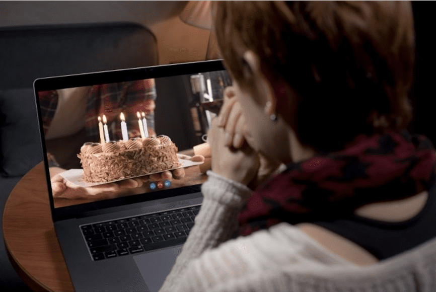 a view of a woman from behind as she is presented a cake on the computer, symbolizing a virtual birthday