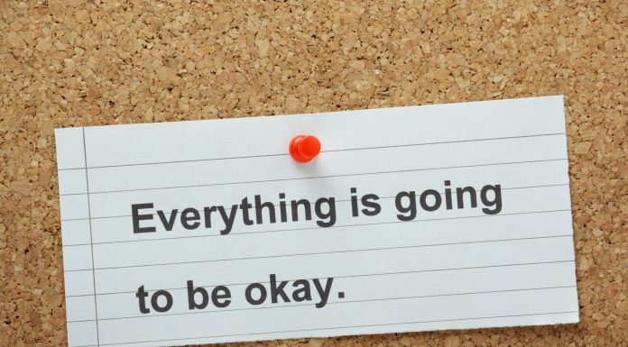 a white notecard that says, "Everything is going to be okay" pinned to a cork board with a red tack.