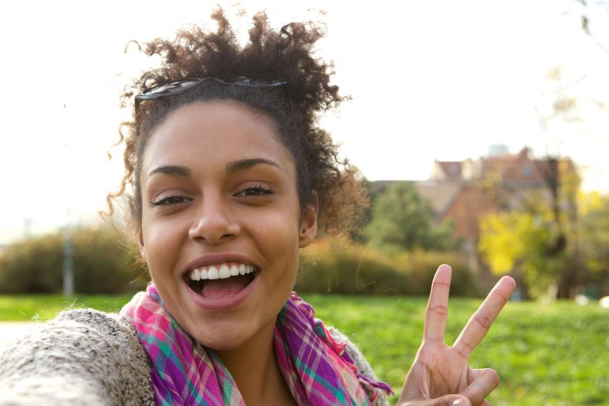 close up of a smiling woman holding up two fingers in a peace sign to symbolize everything is ok