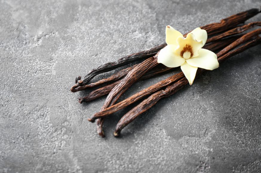 a cluster of vanilla beans with a vanilla flower on top on a marble tabletop
