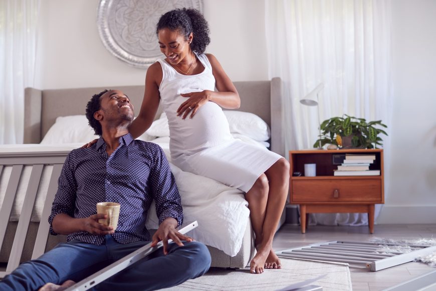 an African American couple setting up a crib in the master bedroom
