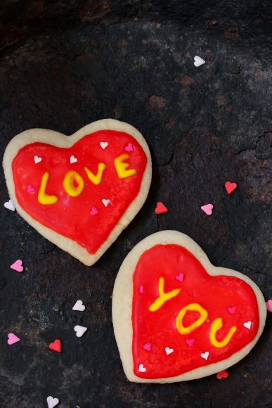 two sugar cookies with red icing, one says "love" in yellow, and the other says "you" in yellow