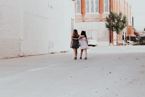 two girls, walking down a street with their arms around each other