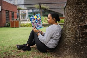 a young adult leaning against a tree as she reads a book about women's history month