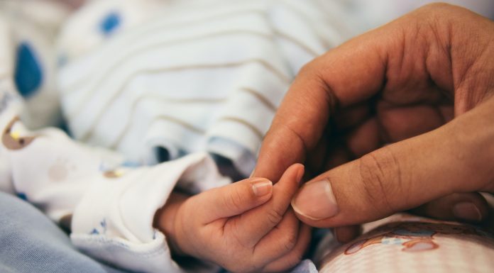 a mom's hand holding her little newborn baby's hand during maternity leave
