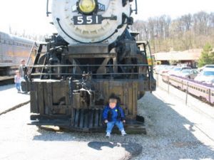 a toddler boy sitting in front of a train at the Transportation Museum in St. Louis