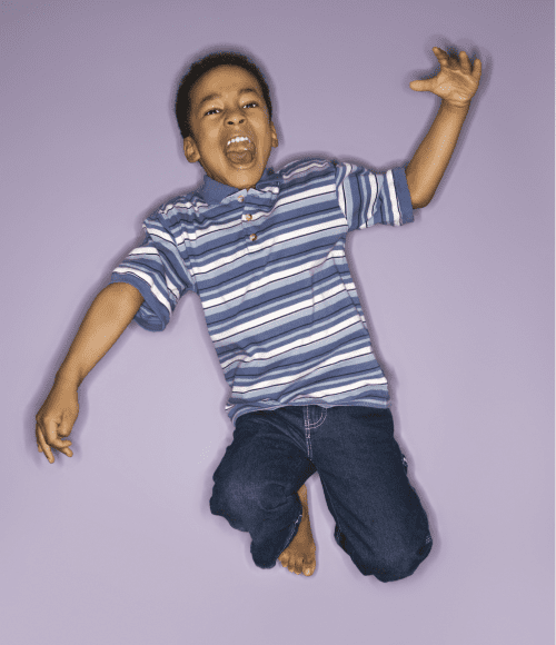 an African American boy in a striped shirt and jeans jumping up into the air as he yells