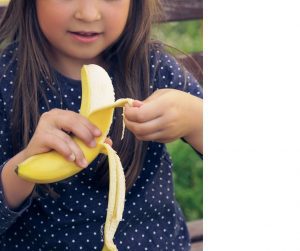 a young girl in a navy dress with white dots on it peeling a banana