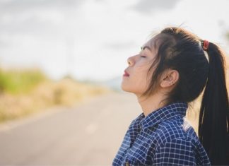 a woman standing at the side of the road with her eyes closed, taking a deep breath