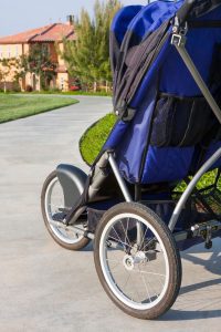 a blue jogging stroller from behind on a sidewalk meandering through a neighborhood