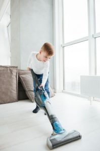 a boy vacuuming the floor with a stick vacuum