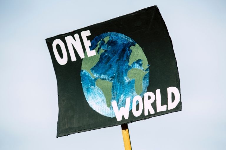 a black sign with the earth on it that says, "one world" held up high against the sky