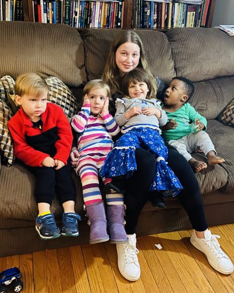 four toddlers and a teenager squeezed together on a couch