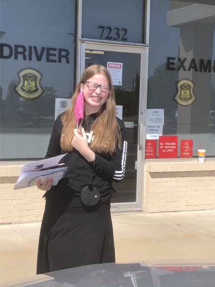 a teen girl standing outside of the driver's exam office holding her new drivers license