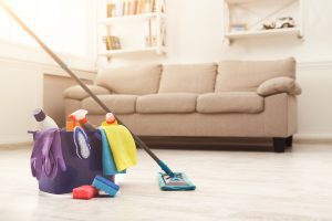 a bucket of cleaning supplies with a mop leaning against it in front of a beige couch
