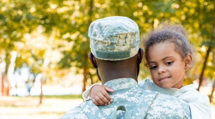 a close up of a military dad from behind as he holds his daughter, whose face we see is smiling