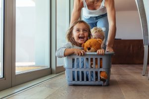 a little boy and girl in a laundry basket, being pushed by their stay-at-home mom