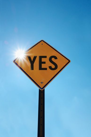 a yellow diamond street sign with the word YES written in black, set against a blue sky