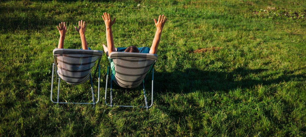a photo from behind of a mom and her son sitting in chairs in the grass with their arms raised up in the air