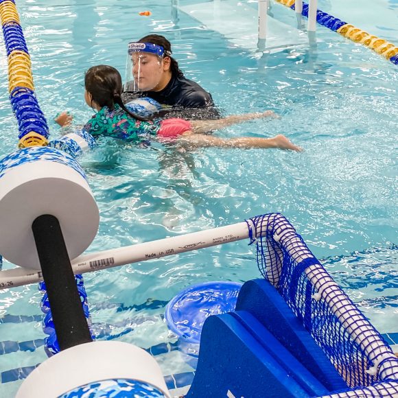 a girl in a bright colored swimsuit with a Foss Swim School swim instructor, learning about water safety in the pool