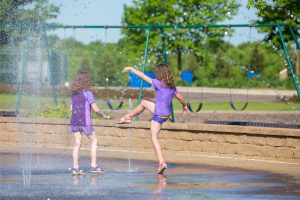 two girls dressed in purple as they play in the water feature at a park