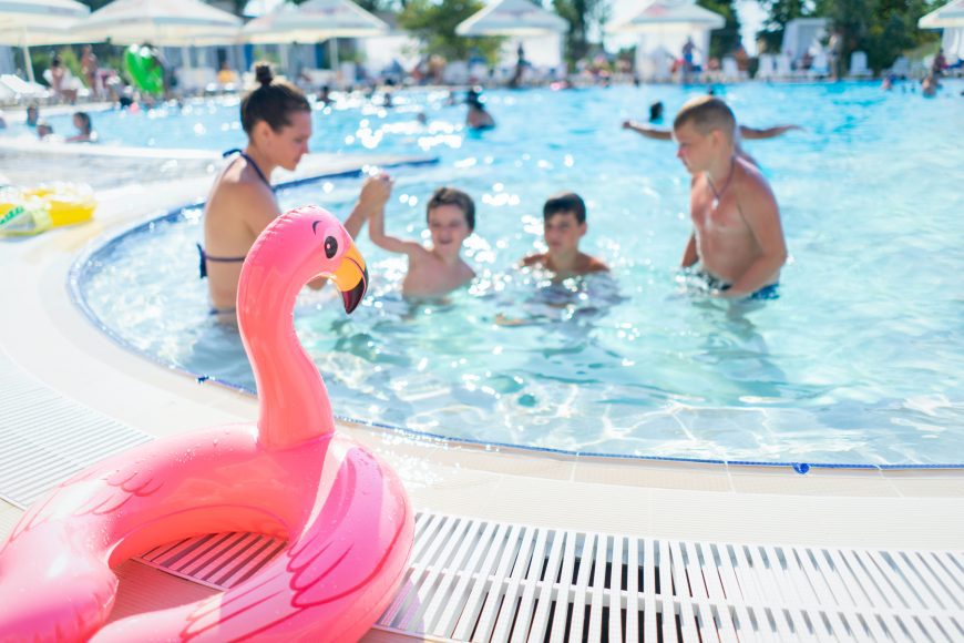 kids swimming at a neighborhood pool with a flamingo floatie on the side of the pool