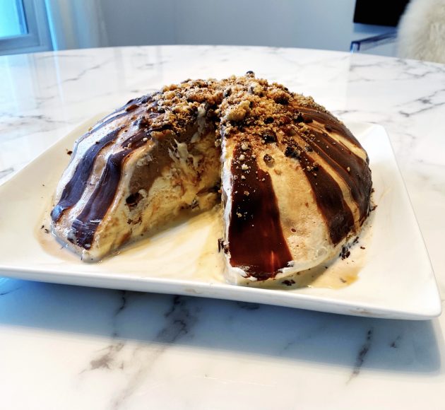 A layered ice cream bombe on a white platter on a marble countertop