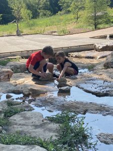 a boy and a girl crouched down as they play in a stream
