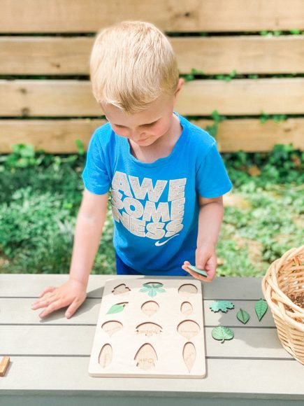 a toddler putting a puzzle together on a table outdoors, enjoying nature