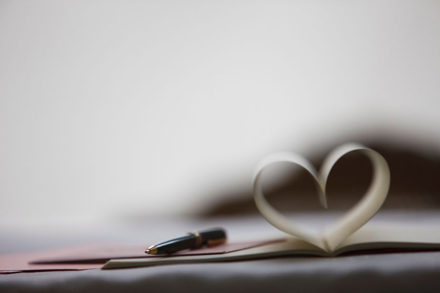 a pen on top of a journal that has two pages folded into the shape of a heart