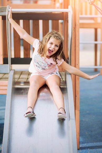 a girl smiling with her arms out as she slides down a metal slide