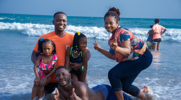 an African American family, posing in the waves on the beach as the mom gives a peace sign