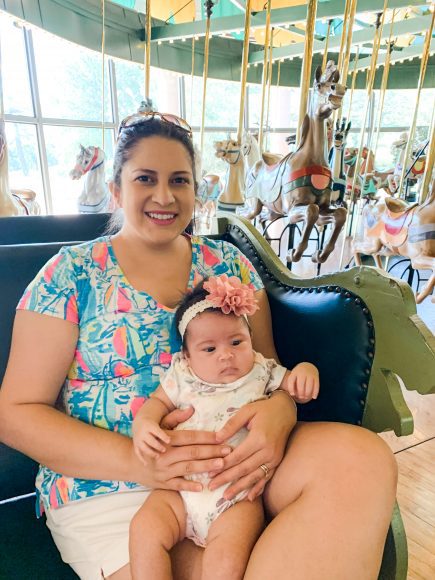 a mom holding her baby girl on her lap at the carousel at Faust Park in Chesterfield, MO