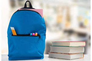 a new backpack filled with school supplies on a table next to a stack of books 