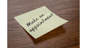 a sticky note on a wooden table that says, “make an appointment"