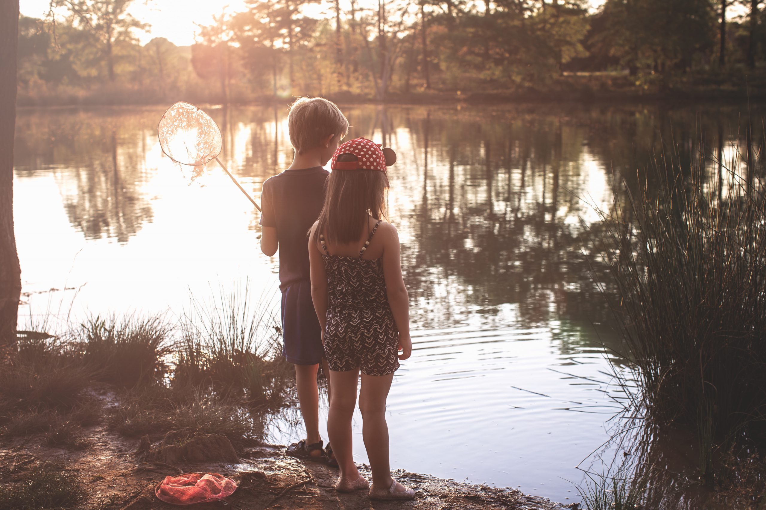 a picture of a girl and a boy holding a fishing net at the edge of a lake