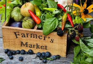a wooden crate etched with the words, “Farmer’s Market” and filled with produce and flowers to represent the Kirkwood Farmer’s Market