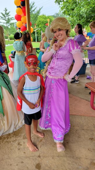 super heroes and princesses visited an event as a young boy poses for a picture