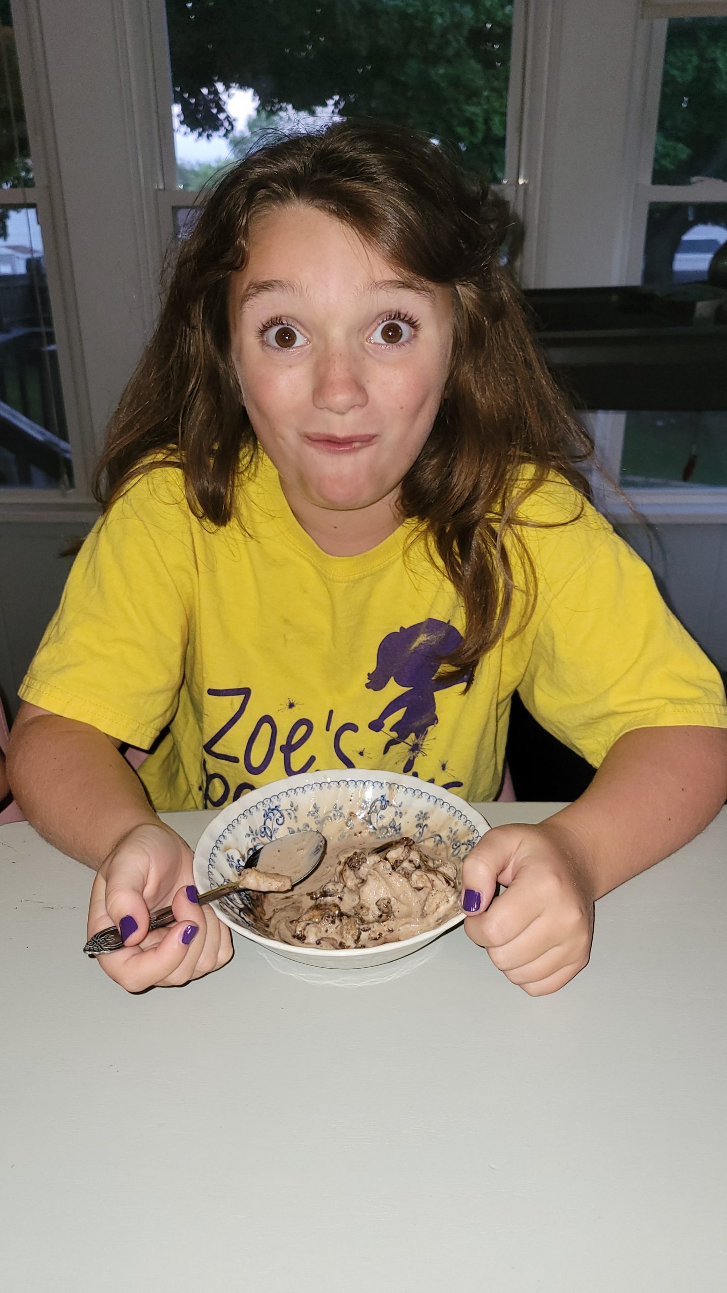 a girl making a silly face as she enjoys a bowl of ice cream