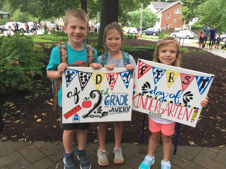 a boy and two girls holding first day of school signs