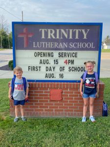 a young boy and his sister standing by the school marquee board for the first day of school