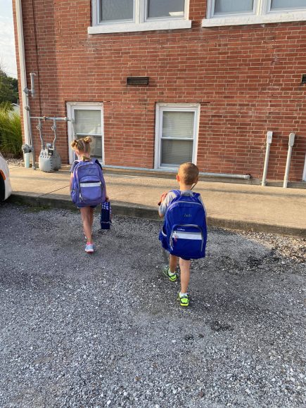 a young girl and her brother, wearing big backpacks as they head back-to-school