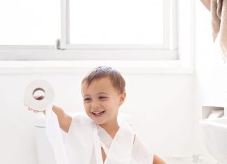 a toddler boy wrapped in toilet paper as he sits on the toilet