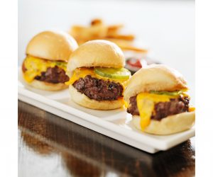 three sliders on a plate with French fries in the background