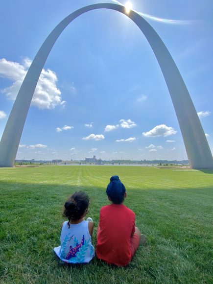 two children sitting in the grass, looking at the St. Louis arch